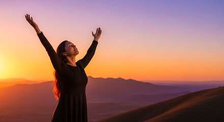 Fototapeta premium A woman raises her arms as the sun sets on a mountain.
