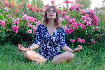 Young woman meditating in lotus position surrounded by blooming roses in a peaceful park