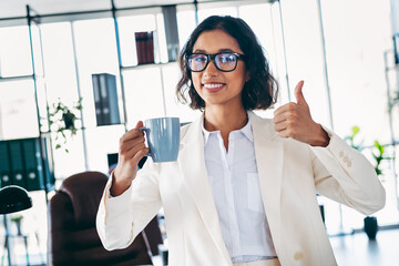 Confident businesswoman smiling in modern office while holding a coffee mug, symbolizing...