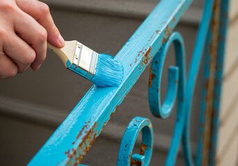 Close-up of brush applying glossy blue paint on a rusty iron railing
