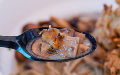 Spoon with cooked mushrooms in broth, close-up of Asian food. Macro photography with texture and warm tones. Ramen