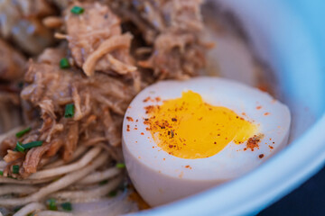 Close-up of ramen with noodles, shredded meat, and marinated egg with creamy yolk and spices. Homemade Japanese food.