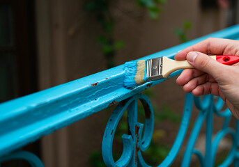 Close-up of brush applying glossy blue paint on a rusty iron railing