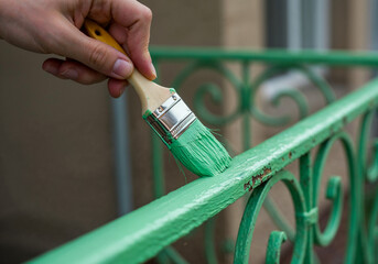 Hand painting old iron railing with green protective paint during restoration