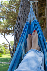 Close-up of women's feet with red pedicure relaxing in a hammock in nature