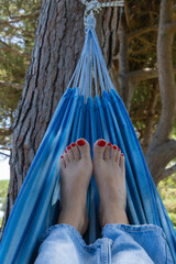 Close-up of women's feet with red pedicure relaxing in a hammock in nature