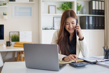 Businesswoman talking on phone while calculating financial data at her desk.