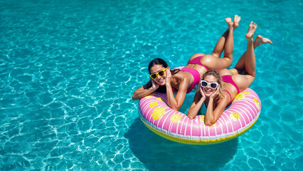 Young women in early twenties on pink inflatable pool ring floating on water. Space for text. Beach mood