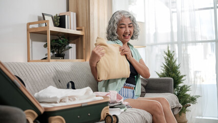 Senior woman packing suitcase with clothes and essentials, getting ready for a vacation.
