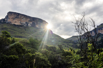 The last rays of sunlight as the sun start to disappear behind one of the tall sandstone cliffs in the Drakensberg mountains in Royal Natal, South Africa