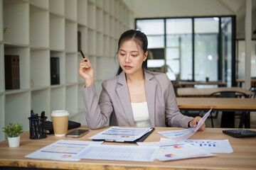 Focused businesswoman analyzing financial charts and reports in modern office.