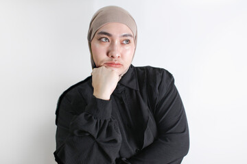 Pensive Muslim woman in hijab resting her chin on hand, looking away thoughtfully. Concept of...