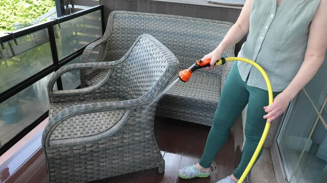 Anonymous cleaning, hose water washing wicker furniture from summer. Structures in backyard. Cleanliness and order.