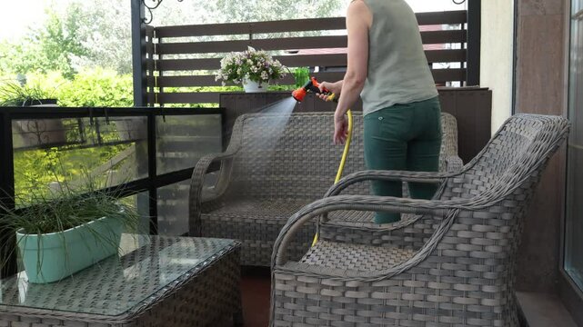 Anonymous cleaning, hose water washing wicker furniture from summer. Structures in backyard. Cleanliness and order.