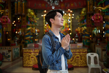 Tourist man with backpack praying respectfully at a vibrant Chinese temple.