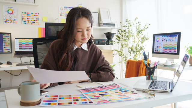 Female graphic designer analyzing color samples and design layouts in a creative workspace.