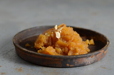Rich and traditional Indian dessert moong dal halwa – golden yellow lentil pudding made with ghee, sugar, and cardamom – garnished with dry fruits, served hot in bowl, festive sweet