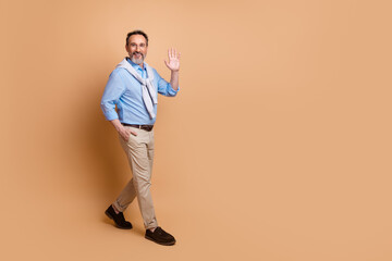Mature businessman waving with a welcoming gesture in casual yet stylish attire against a beige...