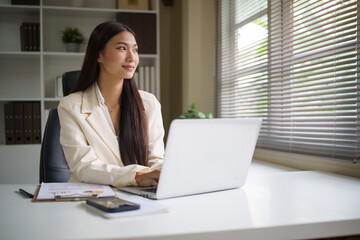 Thoughtful businesswoman sitting at her desk, looking out the window while reflecting on ideas and planning her strategy.