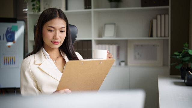 Confident businesswoman holding coffee cup and analyzing financial data in a bright modern office.
