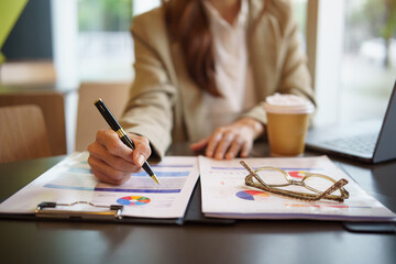 Close up of  businesswoman hand holding a pen and analyzing charts and graphs.