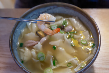 A bowl of soup with a shrimp in it. The soup is yellow and has a lot of green onions in it