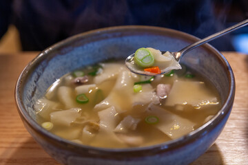 A bowl of soup with a shrimp in it. The soup is yellow and has a lot of green onions in it