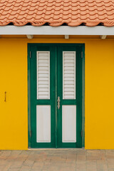 Bright green door contrasts with vibrant yellow wall under a tiled roof in a tropical setting