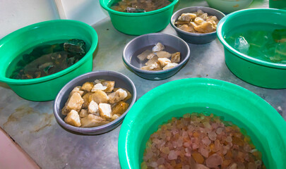 Exhibition of mined precious stones, many types and colors in bowls with water on a table, Moonstone Mine tour, Sri Lanka.