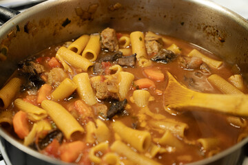 Chef preparing delicious beef stew with rigatoni pasta and vegetables
