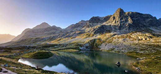 Bergsee mit Spiegelung in den Schweizer Alpen im warmen frischen Morgenlicht mit klarem blauen Himmel, Julierpass, Schweiz