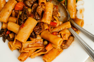 Delicious pasta with beef stew and vegetables being mixed with silver cutlery