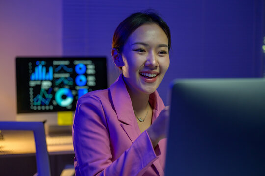 Asian businesswoman working late using laptop and smiling at online meeting - Powered by Adobe