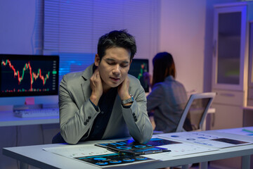 Tired businessman suffering from neck pain while working late at night in office