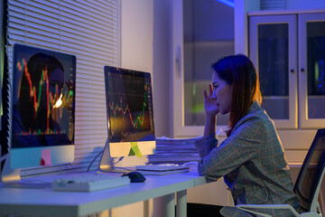 Stressed businesswoman analyzing declining stock market chart on computer screens in office at night