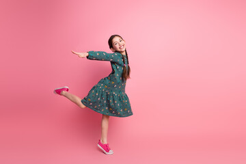 Young girl in a floral dress posing joyfully on a pink background, showcasing bright fashion style...