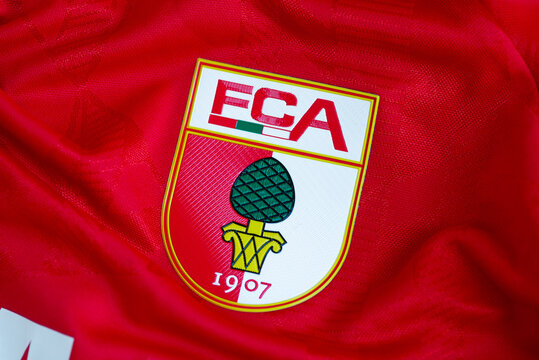 Kyiv, Ukraine - July 7, 2025: Close-up of FC Augsburg football club logo on a red jersey, featuring team crest with pinecone emblem and founding year 1907.