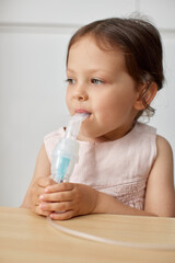 cute little toddler girl inhaling medicine on nebulizer and holding it on her own