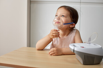 cute little toddler girl inhaling medicine on nebulizer and holding it on her own