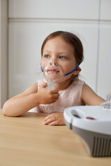 cute little toddler girl inhaling medicine on nebulizer and holding it on her own