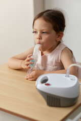 cute little toddler girl inhaling medicine on nebulizer and holding it on her own, portable inhaler...
