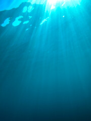 Dark blue ocean surface seen from underwater. Abstract waves underwater and rays of sunlight shining through, Sun light rays undersea deep, Underwater background with sea bottom, Mediterranean sea.