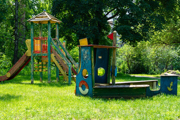 Old abandoned playground among green trees in summer