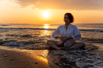 Woman meditating at sunrise on the beach, embracing slow living
