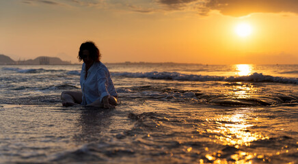 Woman meditating on the beach at sunrise embracing slow living