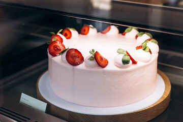 Strawberry cake on display in pastry shop window behind glass showcase.