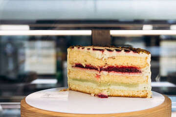 Sliced sponge cake with raspberry and pistachio layers in café display.