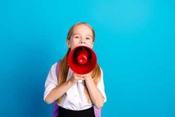 Charming young schoolgirl using a red megaphone against blue background, promoting education and...