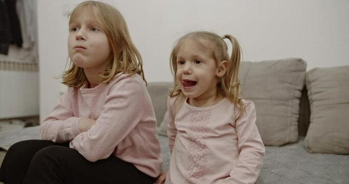 Two young sisters spend quality time together at home, making silly faces and picking their noses.