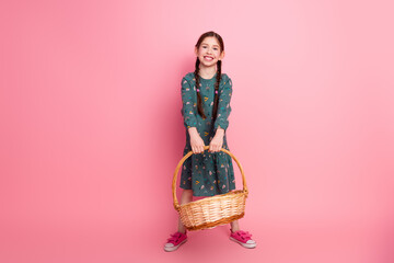 Smiling young girl in casual dress holding a farmer basket against a pink background expressing...